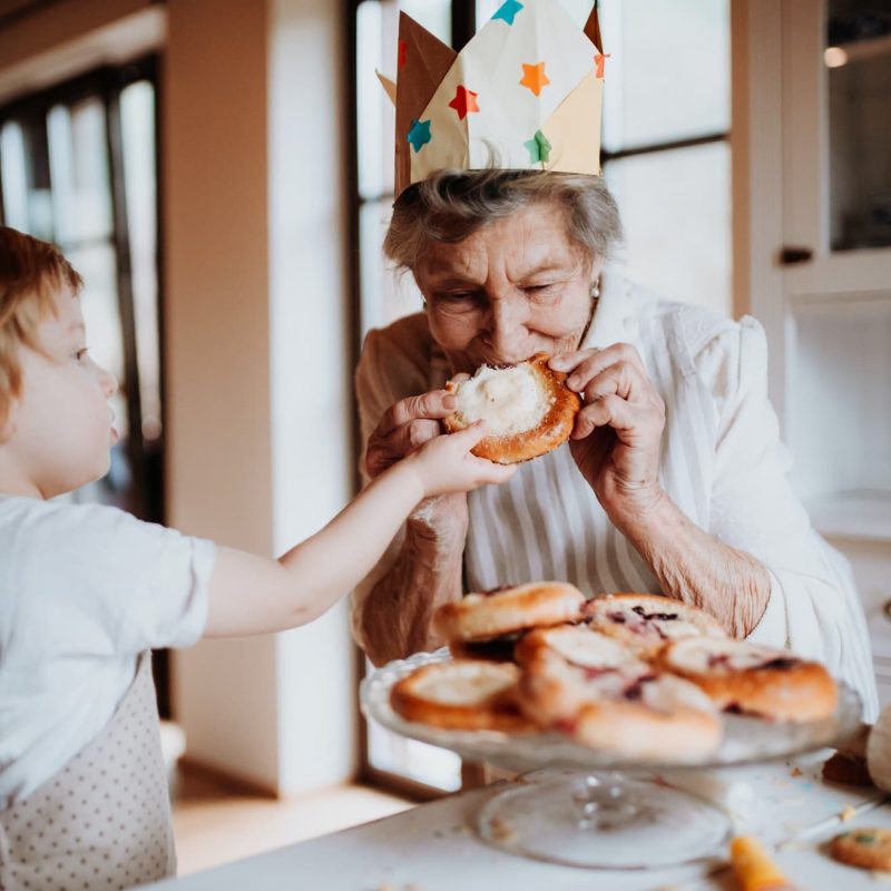 Senior grandmother with small toddler boy making and eating cakes at home.
